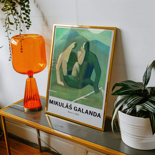 Framed artwork on a table with an orange lamp and plants