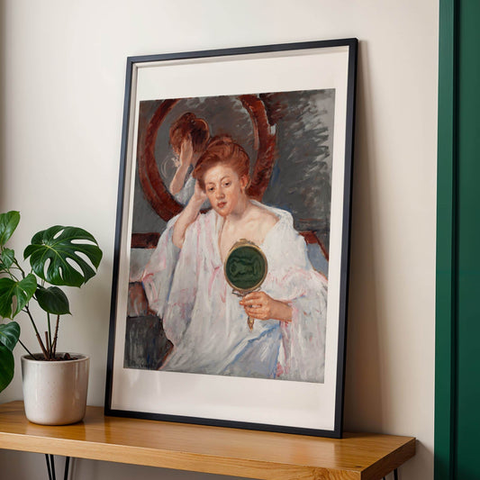 Framed painting of a woman holding a mirror on a wooden table with a plant in the background