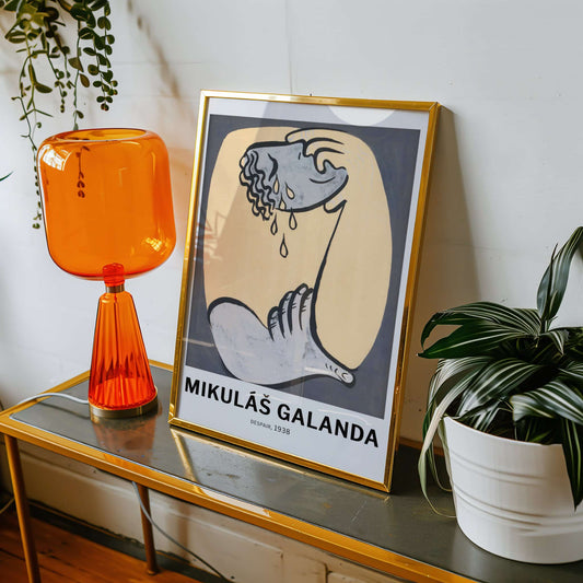 Framed artwork on a table with an orange lamp and plant
