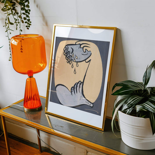 Framed artwork on a table with an orange lamp and plant