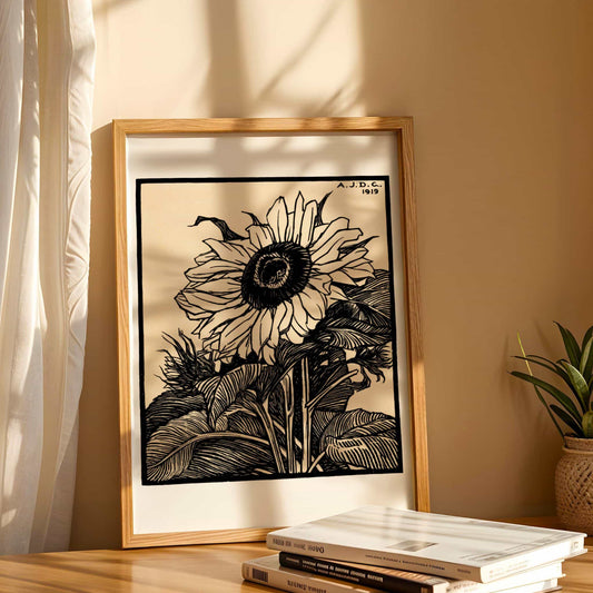 Framed black and white sunflower artwork on a wooden surface with a plant in the background.
