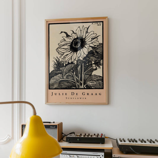 Framed artwork of a sunflower by Julie De Graag on a wall above a desk with musical equipment.