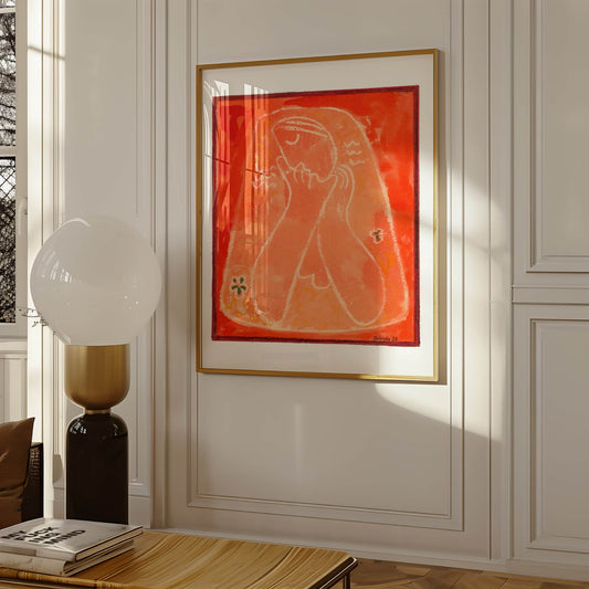 Framed abstract artwork on a wall with a lamp and books on a table below.