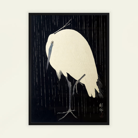 Framed artwork of a white bird in a rainstorm with a black background. Egret in the Rain by Ohara Koson