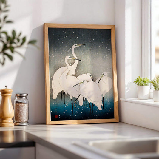 Framed artwork of white birds on a dark background in a kitchen setting. Egrets in the Snow by Ohara Koson