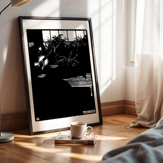 Framed black and white artwork on a wooden surface with a cup of coffee and books. The Guitar by Félix Vallotton